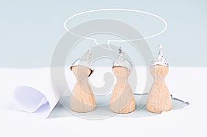 Three wooden figures wearing an alu hat,speech bubble conspiracy theories, tin foil