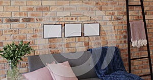 Three wooden frames, plant and sofa with copy space on brick wall