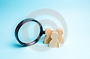 Three wooden human figure stands near a magnifying glass on a blue background. Search for vacancies and work. Human resources,