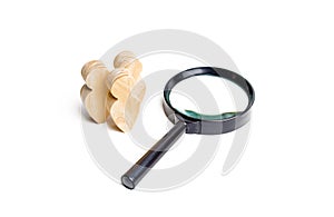 Three wooden human figure stands near a magnifying glass on a white background. The concept of the search for people and workers.