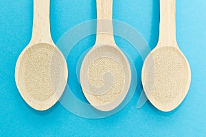 Three wooden spoons with instant dry yeast isolated on a blue background. Yeast is the main ingredient of fresh dough for pastry,