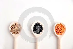 Three wooden spoons with lentils of different varieties, orange, black and brown on a white background. Place for text