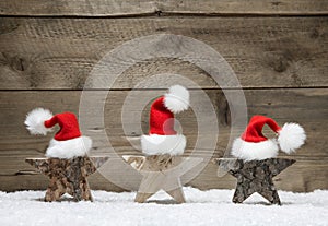Three wooden stars with santa hats on wooden background