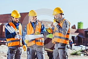 Three workers in hardhats examining building plans and talking on portable radio