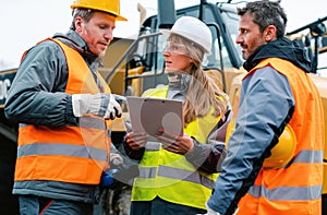 Three workers in a quarry discussing in front of heavy machinery