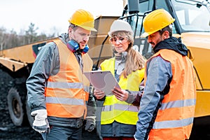 Three workers in a quarry discussing in front of heavy machinery