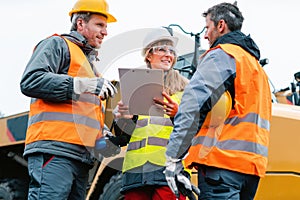 Three workers in a quarry discussing in front of heavy machinery
