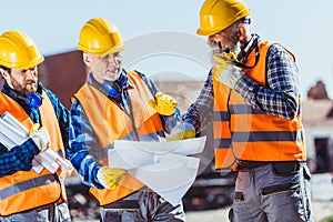 Three workers in uniform examining building plans and talking on portable radio