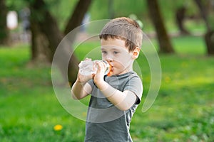 Three year old caucasian toddler boy drinks water from a bottle in the park