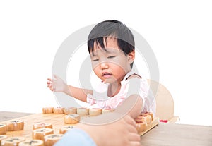 A three-year-old Chinese girl in front of a white background is playing Chinese chess