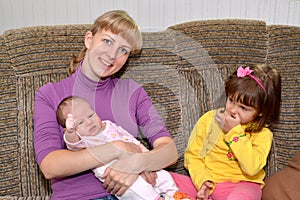 The three-year-old girl with jealousy looks at the little sister on hands at mother