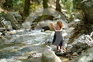 three year old girl playing with an old doll near a river in the beautiful nature of the Dirfi mountain in Eubeoa