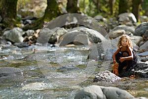 three year old girl playing with an old doll near a river in the beautiful nature of the Dirfi mountain in Eubeoa