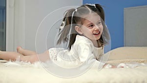 Three-year-old girl plays with feathers, lying on a large bed in the bedroom.