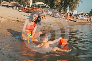 Three year old toddler boy playing with beach toys with mother in the water