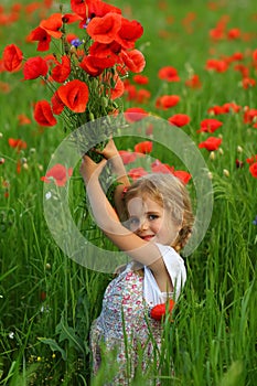 Three year old toddler girl in the summer field of blooming poppies