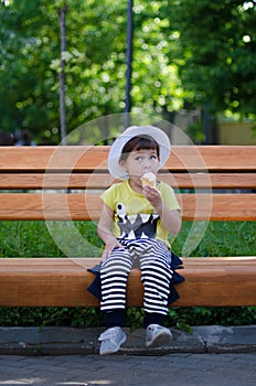 Three years stylish boy seeting on a bench in the park and enjoing an ice cream