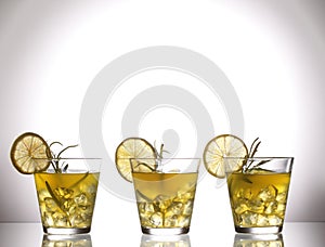 Three yellow cocktails with lemon and rosemary standing on glass in studio