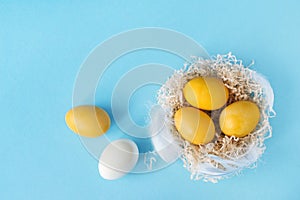 Three yellow eggs in a bird`s nest on a pastel blue background, Easter decor. Flat lay, top view. Copy space