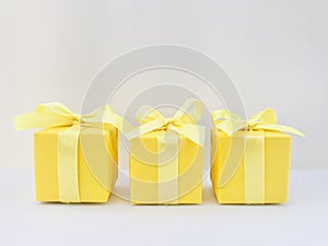 Three Yellow gift boxes on white table, off white background.