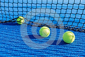 three yellow paddle tennis balls on a blue turf court