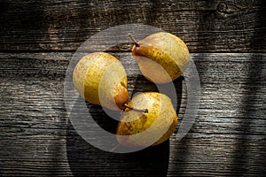 Three yellow pears on a barn wood plank table with shadows from the sun