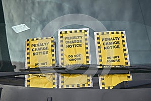 Three yellow penalty charge notices under the wiper blade of a car