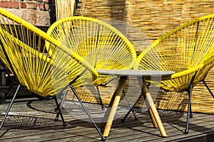 Three yellow plastic chairs  and a table on plank patio