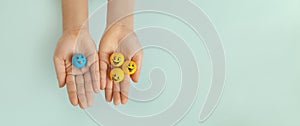 three yellow smiley faces in one hand and one blue smiley face in other child's hand on blue background, copy space