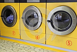 Three yellow washing machines in laundromats