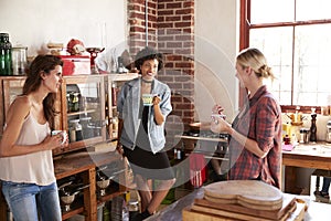 Three young adult girlfriends talk over coffee in kitchen