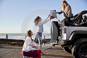 Three young adult girlfriends unloading backpacks from a car