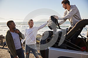 Three young adult male friends unloading backpacks from jeep