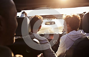 Three young adult men driving in a car with sunroof open