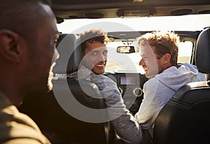 Three young adult men driving with sunroof open, back view