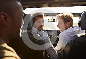 Three young adult men driving with sunroof open, back view photo