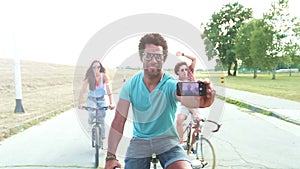 Three young adults on bikes taking selfies with phone, graded