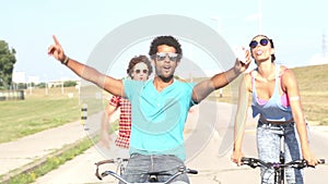 Three young adults cycling and taking selfies with phone, graded