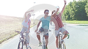 Three young adults having fun cycling and taking selfies with phone, graded