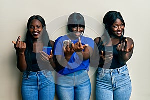 Three young african american friends using smartphone beckoning come here gesture with hand inviting welcoming happy and smiling