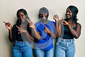 Three young african american friends wearing casual clothes smiling and looking at the camera pointing with two hands and fingers