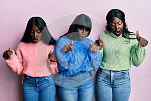 Three young african american friends wearing wool winter sweater pointing down with fingers showing advertisement, surprised face