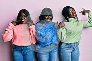 Three young african american friends wearing wool winter sweater smiling cheerful showing and pointing with fingers teeth and