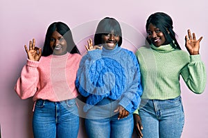 Three young african american friends wearing wool winter sweater smiling positive doing ok sign with hand and fingers