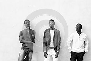 Three young African men hanging out against concrete wall outdoors