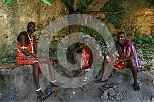 Three young Africans, Masai clothing, rest in the shade.