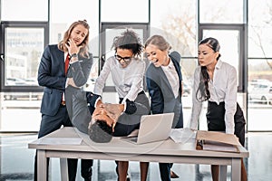 Three young angry businesswomen punishing businessman lying on table photo
