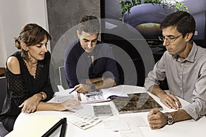 Three young architects discussing together inside a conference room the new interior design concept for a brand presentation.