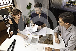 Three young architects discussing together inside a conference room the new interior design concept for a brand presentation.