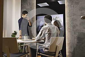 Three young architects discussing together inside a conference room the new interior design concept for a brand presentation.